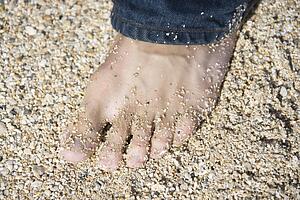 Close up of male foot wearing jeans on sandy beach 