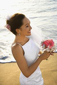 Young adult female bride holding bouquet on beach