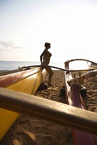 Silhouette of sexy woman in bikini beside outrigger canoe on beach 