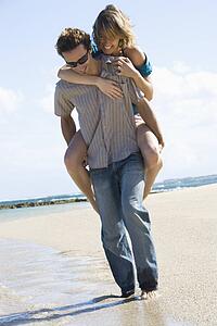 Man giving woman piggyback ride on beach 