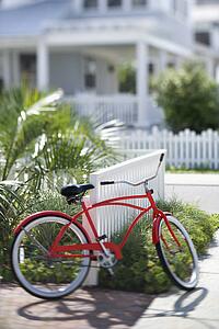 Red beach cruiser bicycle propped against fence in front of house