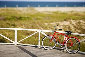 Red beach cruiser bicycle leaning against walkway rail on beach on Bald Head Island, North Carolina.