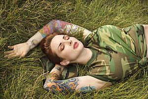 Attractive tattooed Caucasian woman in camouflage lying on grass 