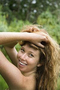 Woman in lush forest holding up long wavy hair
