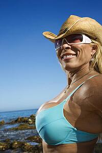 Close up of pretty Caucasian mid adult woman bodybuilder in bikini on beach.