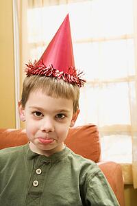 Boy wearing party hat pouting and looking at viewer
