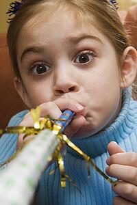 Caucasian girl blowing noisemaker and making facial expression.