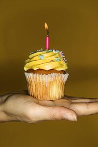 Caucasian prime adult female hand holding cupcake with lit candle.