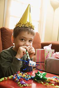 Boy at birthday party looking at viewer blowing noisemaker