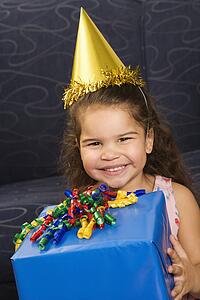 Girl wearing party hat holding birthday present smiling and looking at viewer