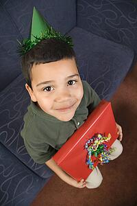 Boy wearing party hat holding birthday present looking up 