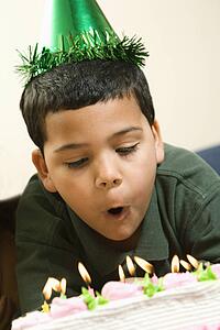 Hispanic boy wearing party hat blowing out candles on birthday cake.