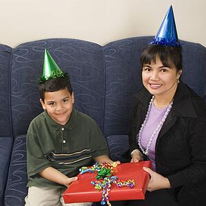 Mother and son wearing party hats holding birthday presents smiling and looking at viewer