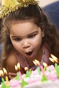 Girl wearing party hat blowing out candles on birthday cake
