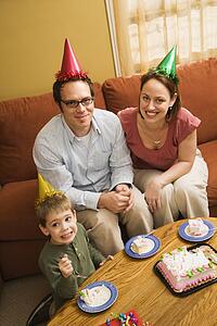 Boy and parents in party hats eating birthday cake