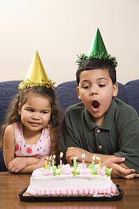 Girl and boy wearing party hats preparing to blow candles out on birthday cake