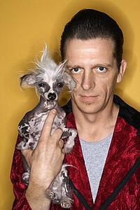 Male wearing velvet and holding Chinese Crested dog