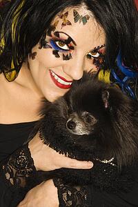 Smiling Caucasian woman in unique makeup holding black Pomeranian dog.