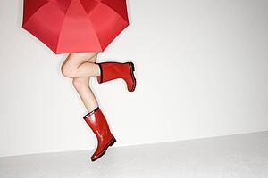Legs of young woman in red boots holding red umbrella and jumping