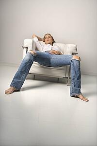 Woman in blue jeans lounging in chair.