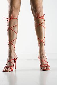Woman's legs and feet wearing sexy red high heel shoes that lace up to her knees.