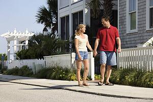 Mid-adult couple walking on suburban sidewalk holding hands