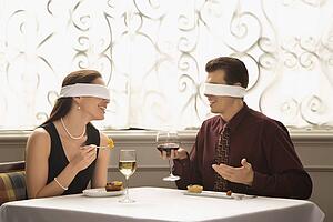 Mid adult couple dining in a restaurant with blindfolds over eyes