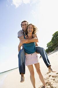 Woman giving man piggyback ride on beach