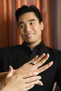 Female admiring engagement ring with male in background
