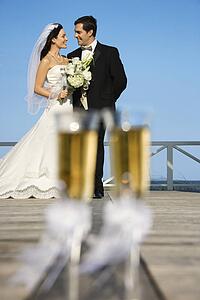 Pair of flute glasses of champagne with Caucasian bride and groom in background.
