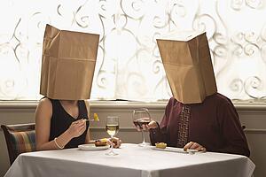 Couple dining in a restaurant with paper bags over heads