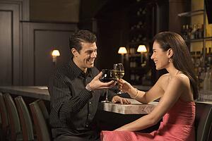 Couple at bar toasting wine glasses and smiling