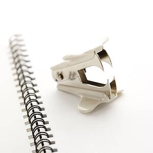 Staple remover on top of an open spiral bound notebook.