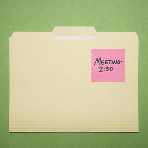 Folder with pink sticky note reminder for a meeting on a green background.