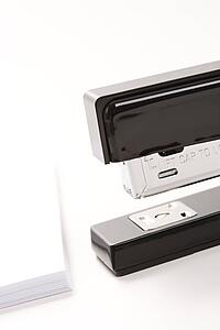 Close up of black stapler on white background with stack of paper