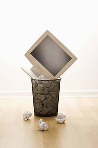 Computer monitor in trash can surrounded by crumpled up paper