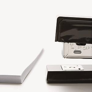 Close up of black stapler on white background with stack of paper.