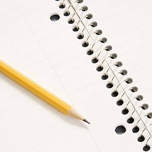Sharp pencil placed on open spiral bound notebook
