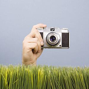Male hand holding vintage camera with grass in foreground
