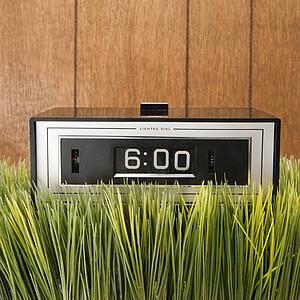 Studio shot of retro alarm clock placed in grass with wood paneling in background.