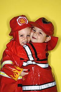 Twin boys dressed as firemen hugging against yellow background
