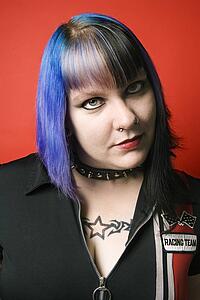 Portrait of woman with blue hair, tattoo, and spike collar against red background