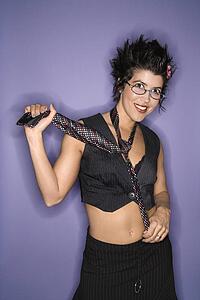 Portrait of smiling Hispanic woman wearing eyeglasses and necktie with exposed midriff standing against purple background.
