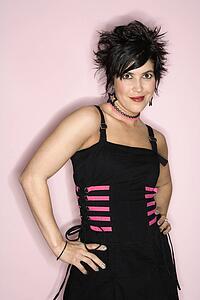 Portrait of Hispanic woman standing against pink background with hands on hips.