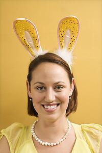 Caucasian mid adult woman wearing rabbit ears and looking at viewer.