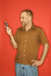 Caucasian man smiling and looking at cellphone standing against orange background.