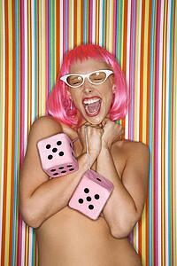 Portrait of attractive Caucasian young adult woman wearing pink wig against striped background holding large pink dice and making sassy expression.