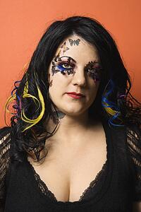 Caucasian woman with unique makeup and hair against orange background.