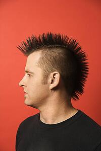 Profile portrait of Caucasian man with spiked mohawk against orange background.