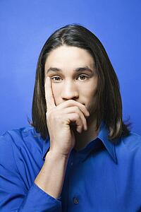 Portrait of teen boy with hand covering chin and finger on side of face against blue background